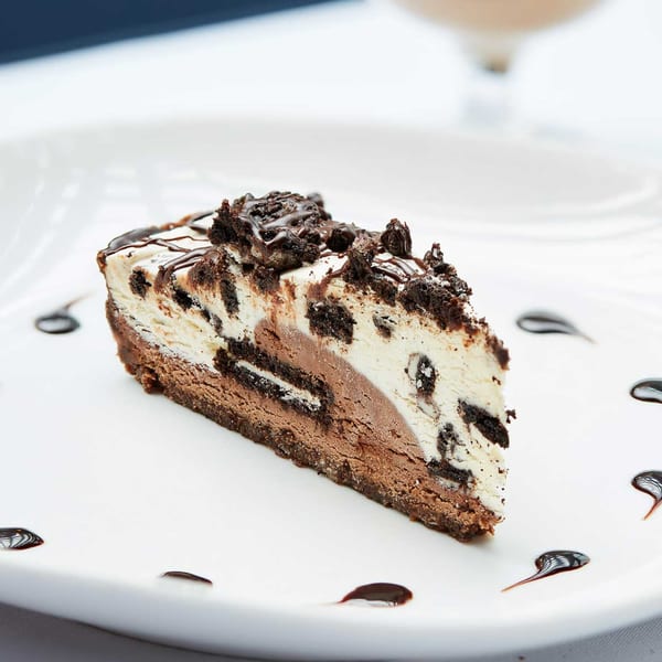 A slice of chocolate and vanilla ice cream cake with cookie pieces and chocolate drizzle.
