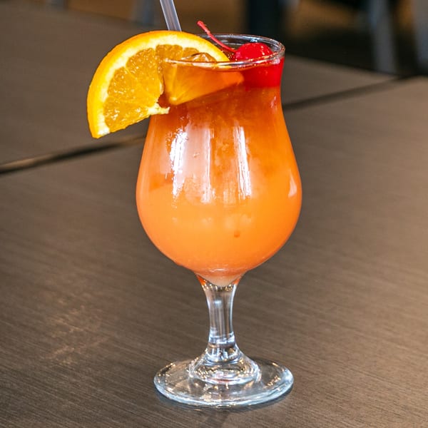 A vibrant orange and red cocktail, garnished with an orange slice and cherry, on a dark wooden table.