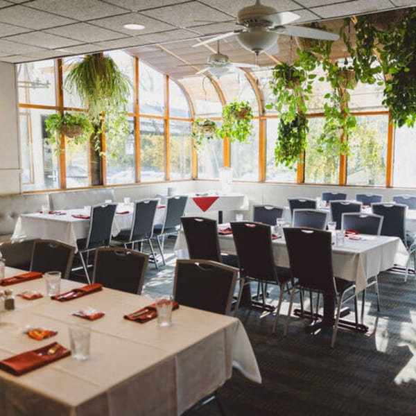 Bright, spacious dining room with set tables, large windows, hanging plants, and ceiling fans.