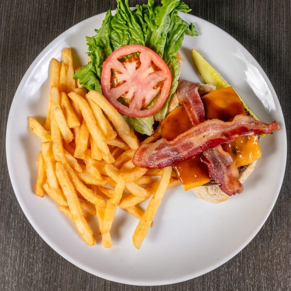 Bacon cheeseburger with lettuce, tomato, and a side of golden french fries and a pickle.