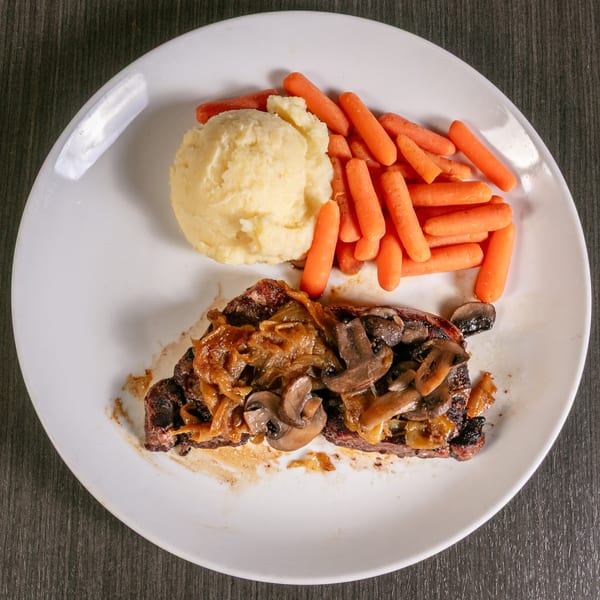 Steak topped with caramelized onions and mushrooms, served with mashed potatoes and baby carrots.
