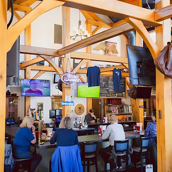 Patrons seated at the bar of the Post Office Pub, with TVs and wooden beams overhead.