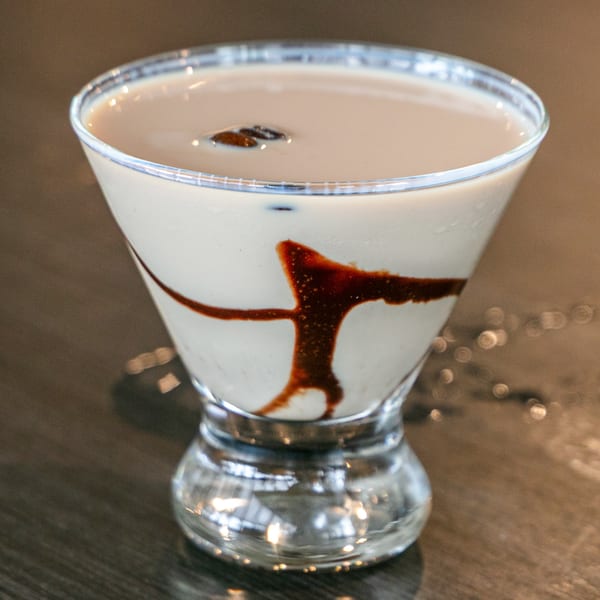 A creamy Post Office Pub cocktail with chocolate drizzle and coffee beans in a martini glass.
