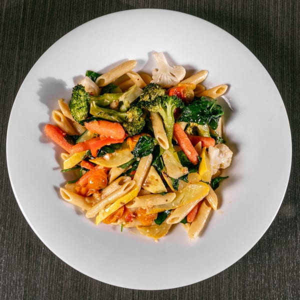 Penne pasta with broccoli, carrots, squash, and spinach on a white plate.