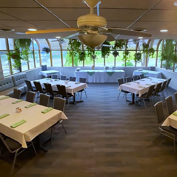 Spacious dining room at Post Office Pub with set tables, ceiling fans, and large windows with hanging plants.