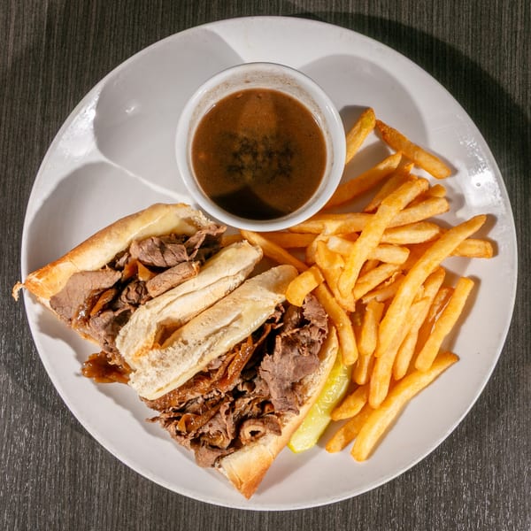 Post Office Pub's American French dip sandwich with fries, pickles, and au jus on a white plate.